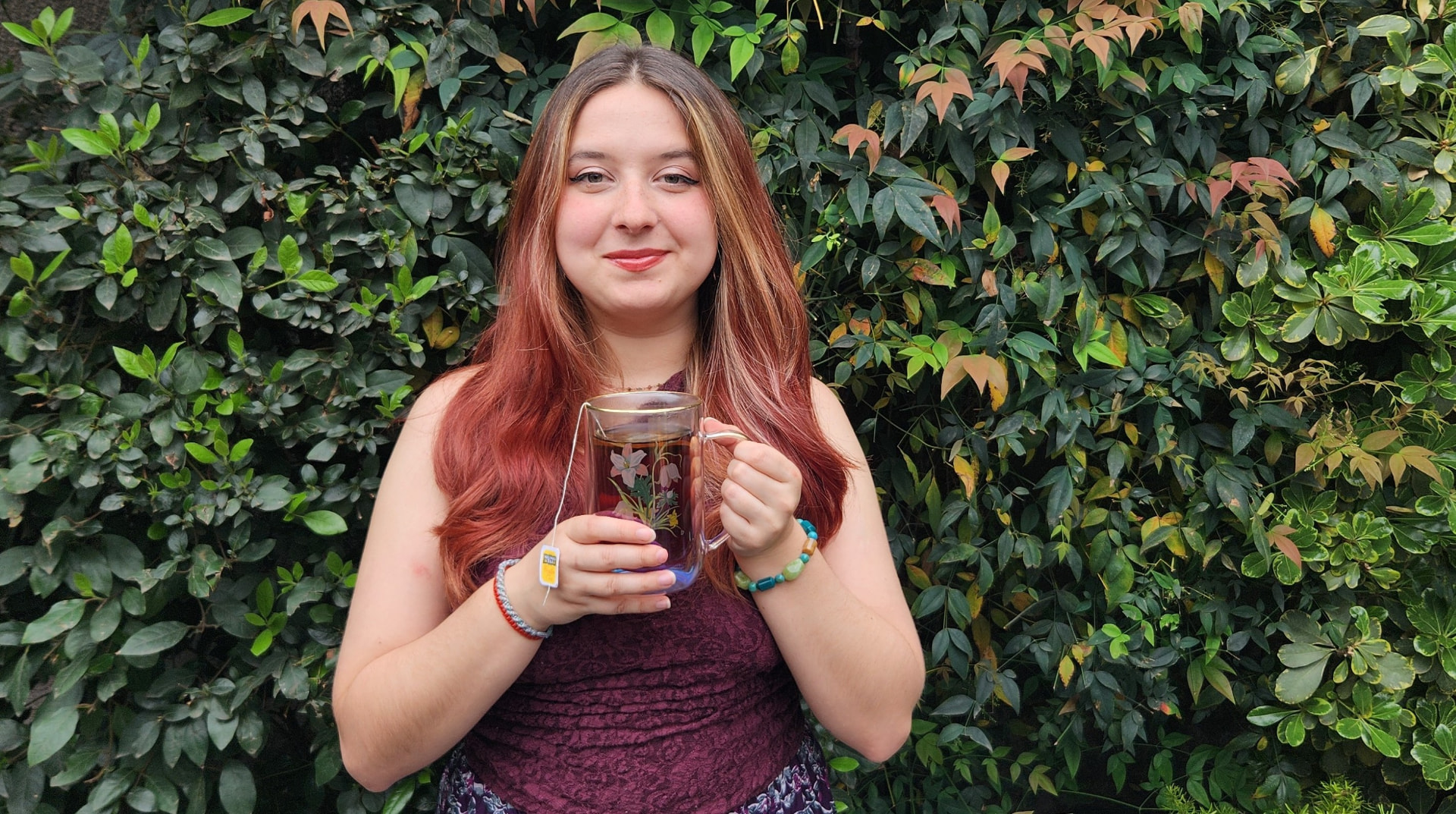 Catalina Wigodski, psicóloga de Psicolumi, sosteniendo una taza de té frente a un muro de vegetación